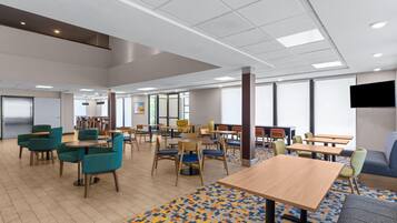 A spacious indoor area with multiple tables and chairs, large windows, and a patterned floor.