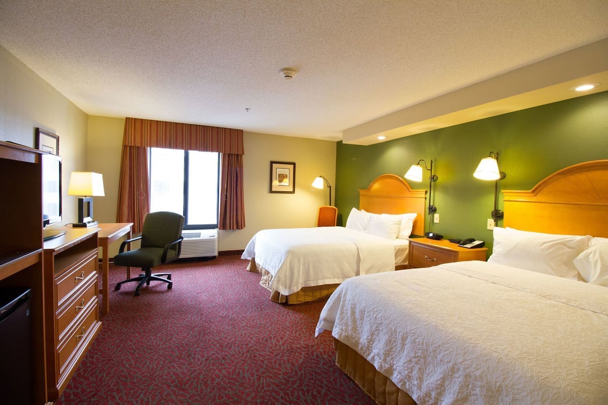 A hotel room with two beds, a desk, a chair, and a window with curtains.