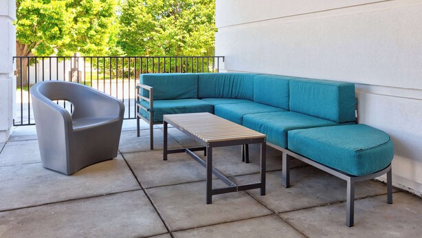 A modern outdoor seating area with a grey chair, a teal sofa, and a wooden table on a concrete patio.