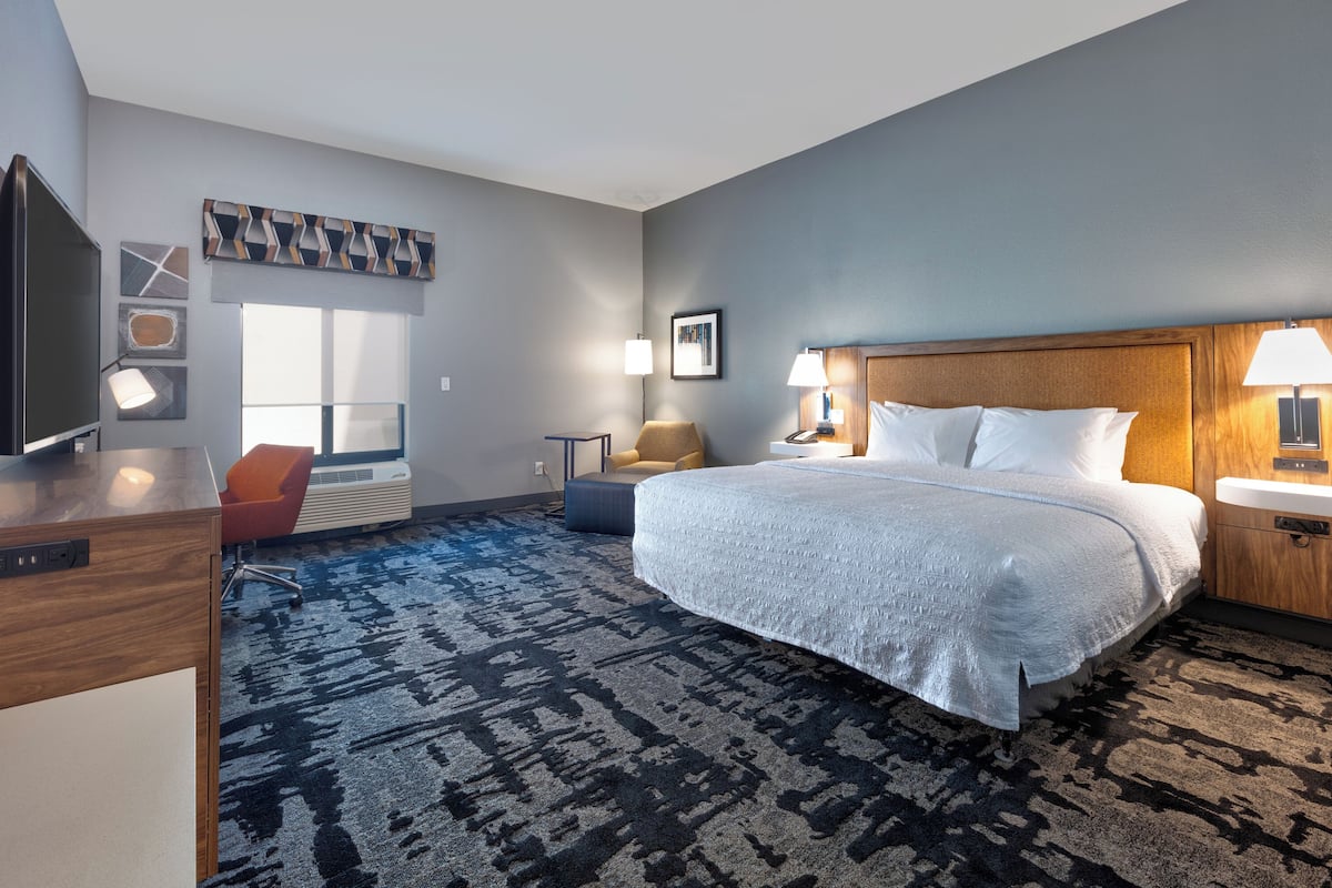 A hotel room with a large bed, a desk, a chair, a TV, and a window.