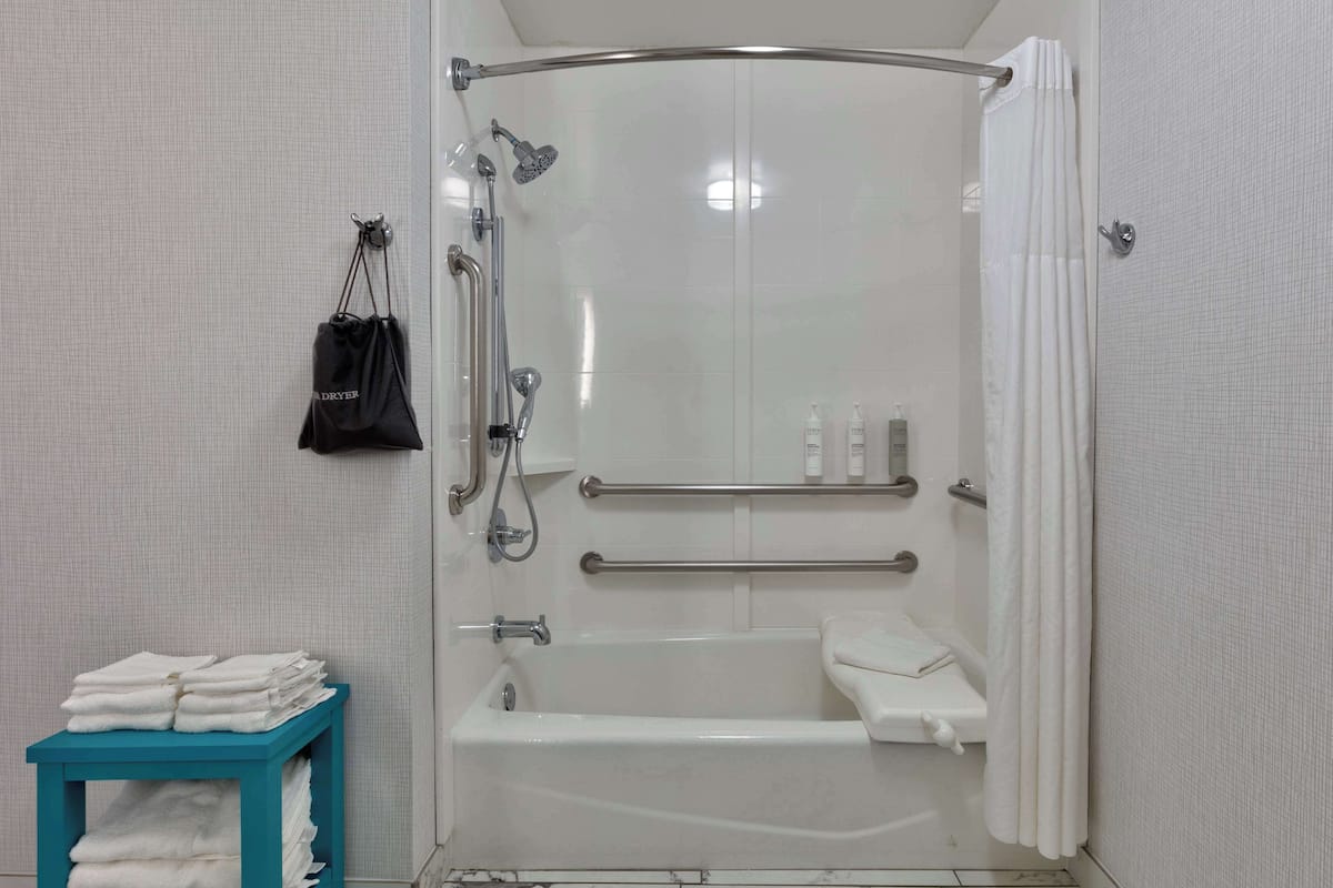 A modern bathroom with a walk-in shower, grab bars, a towel rack, and a blue towel stand.