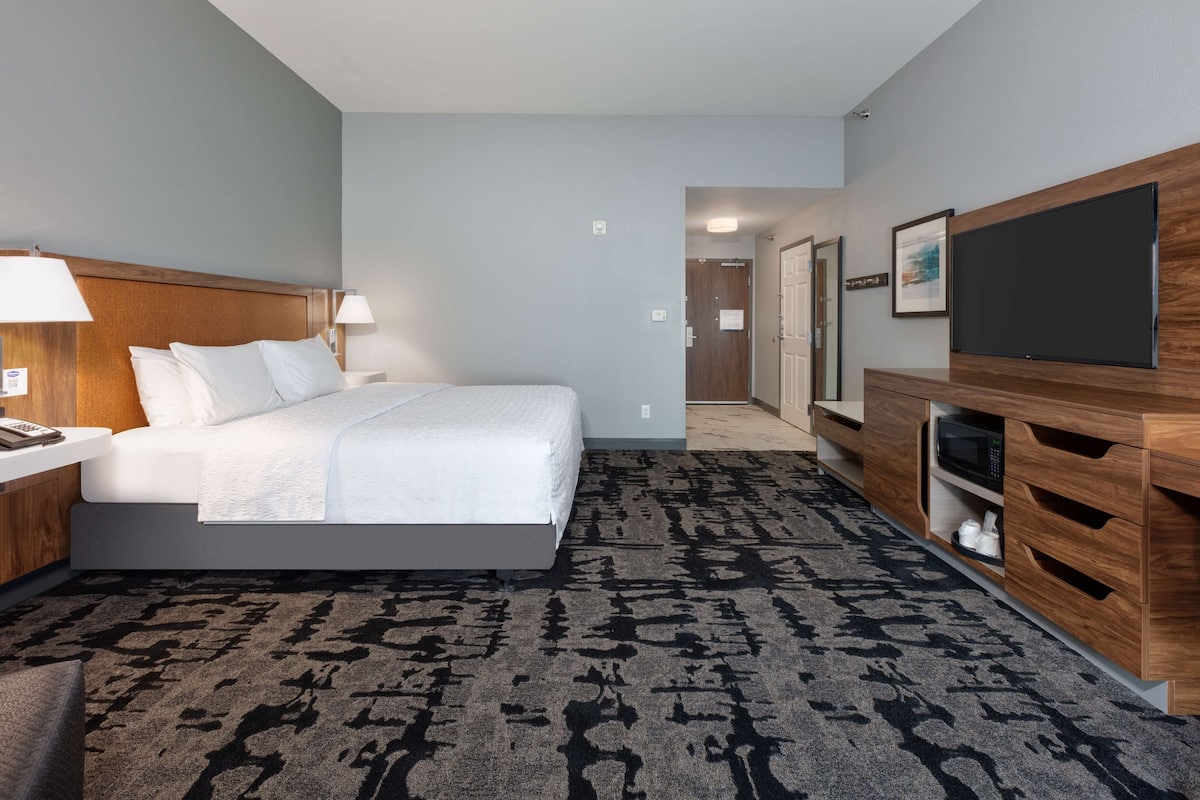 A hotel room with a bed, bedside lamps, a TV, a wooden cabinet, and a carpeted floor.