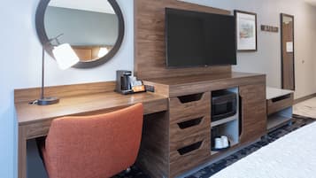 A hotel room with a wooden desk, a flat-screen TV, a coffee maker, a microwave, and a large mirror.