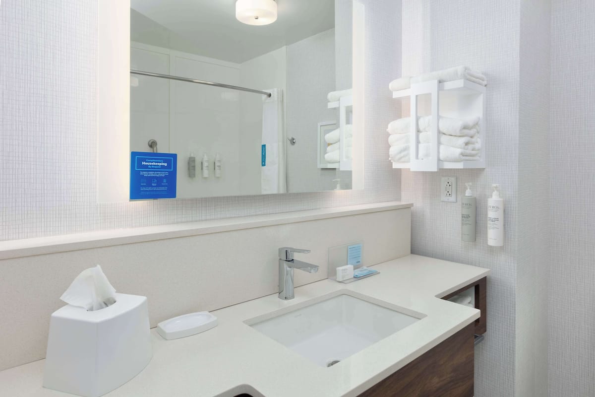 A modern bathroom with a white sink, a mirror, a towel rack, and a hand sanitizer dispenser.