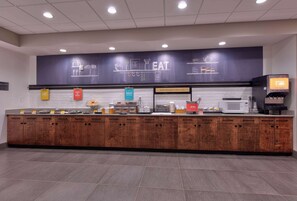 A breakfast bar with a dark counter, wooden cabinets, and a microwave.