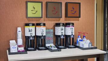 Una estación de café con varios dispensadores, vasos desechables y un molinillo.