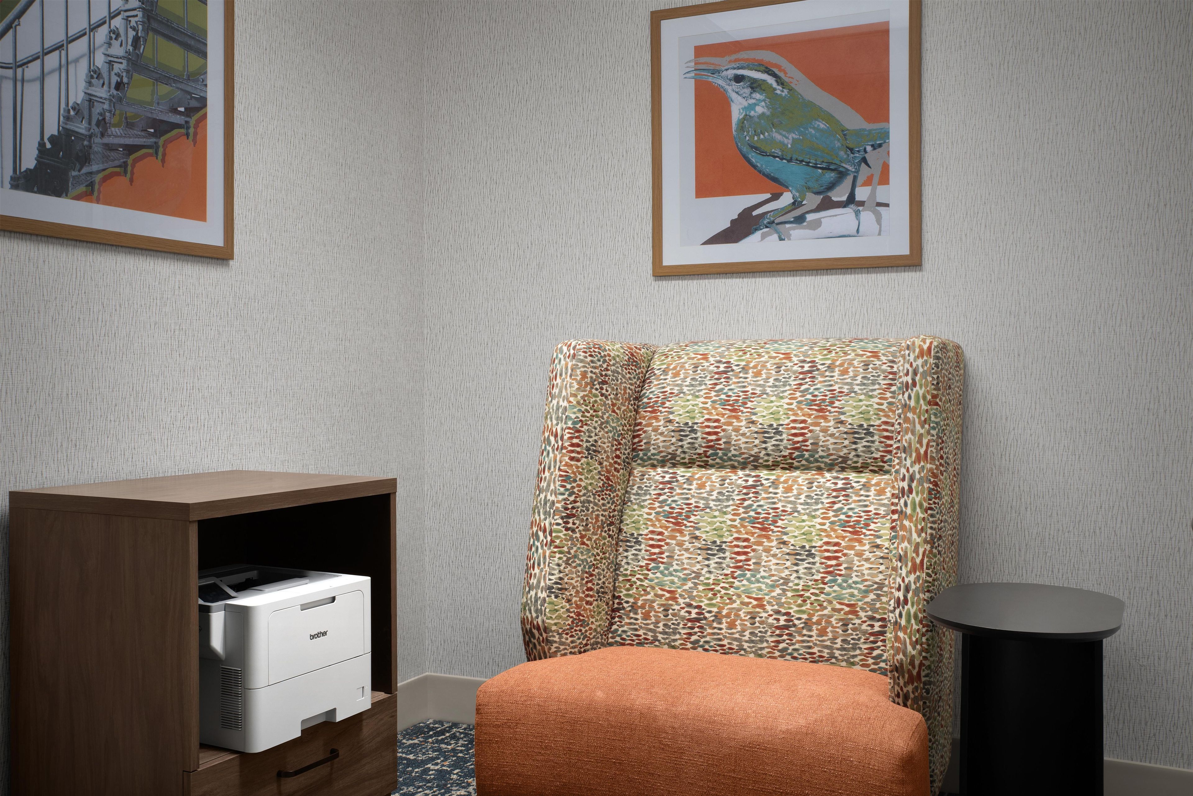 Una habitación con un sillón estampado, una estantería con una impresora y dos cuadros enmarcados en la pared.