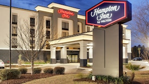A Hampton Inn by Hilton hotel with a modern facade, a welcoming entrance, and a clear sky.