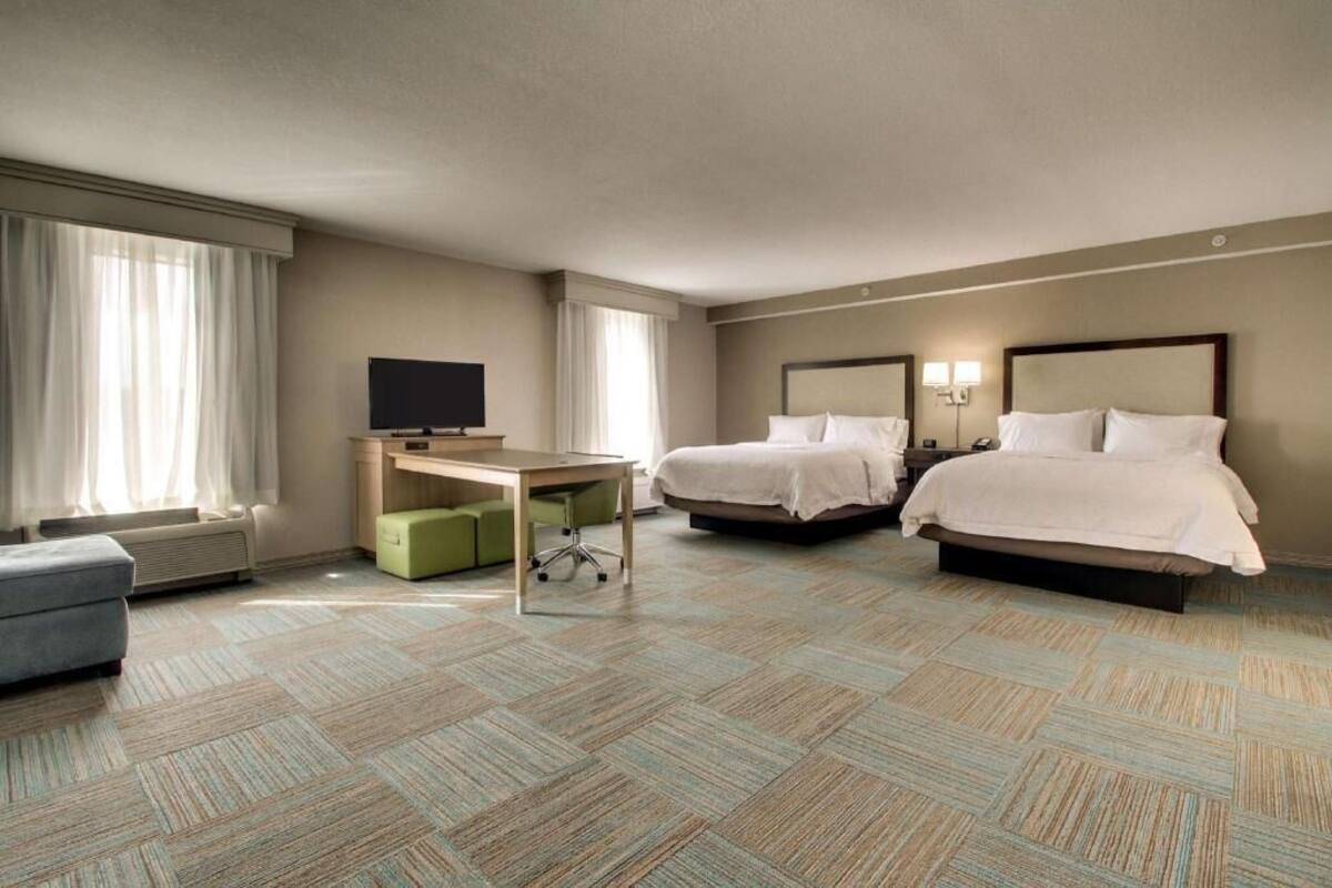 Habitación de hotel con dos camas, un escritorio, un televisor y una ventana con cortinas.