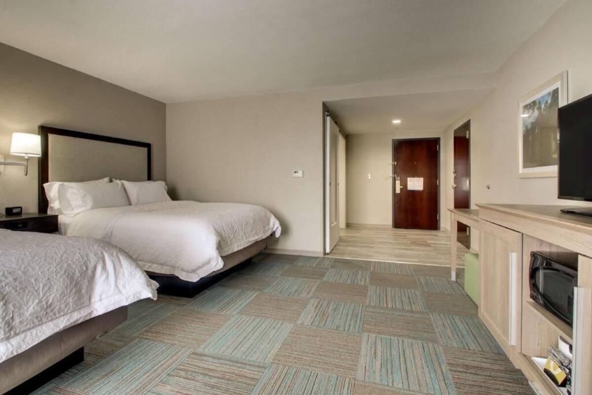 Habitación de hotel con dos camas, televisión, armario y un pasillo.