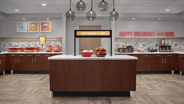 A modern breakfast area with a central island, wooden cabinets, and a sign that reads 'HAPPY BREAKFAST STARTS HERE.'