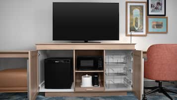 Un mueble moderno para entretenimiento con un televisor de pantalla plana, un refrigerador negro, una cafetera y un microondas.