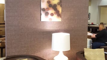 Un área de descanso con dos sillones de cuero marrón, una mesita con una lámpara blanca y una pared con tres paneles cuadrados con estampado de lunares.