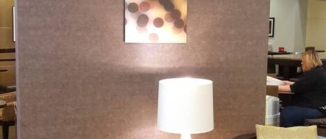 A seating area with two brown leather chairs, a small table with a white lamp, and a wall with three square panels displaying a polka dot pattern.