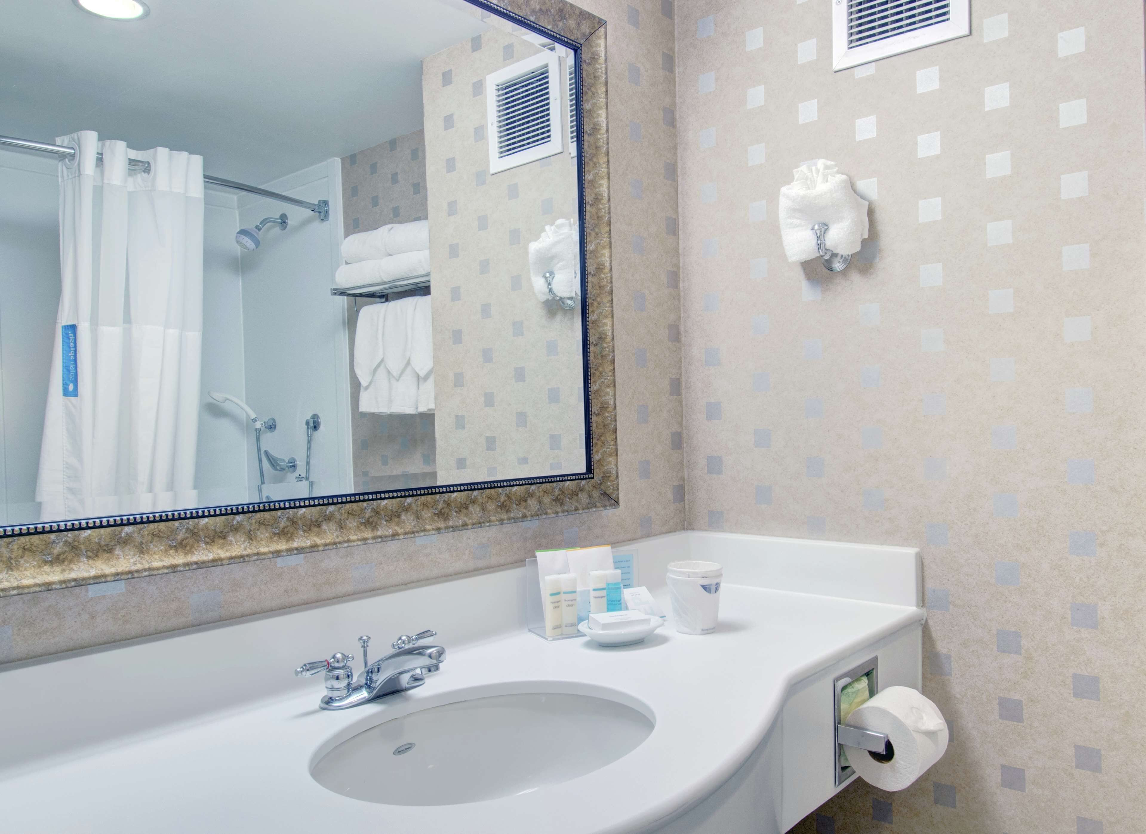 A bathroom with a large mirror, a sink, a shower, and a towel rack.