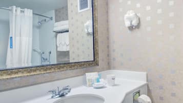A bathroom with a large mirror, a sink, a shower, and a towel rack.