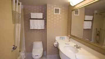Un baño con inodoro, lavamanos y espejo. Hay toallas colgadas en la pared.