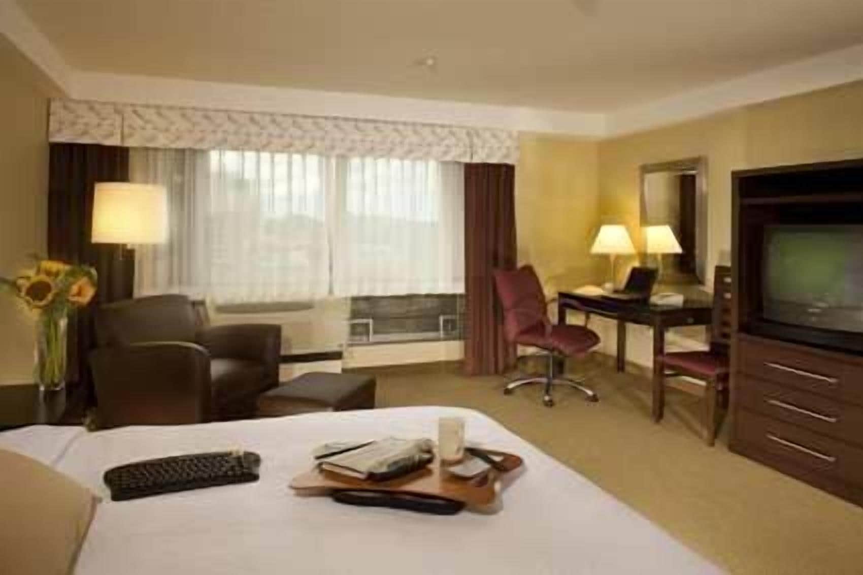 A hotel room with a bed, a desk, a chair, a television, and a window with curtains.