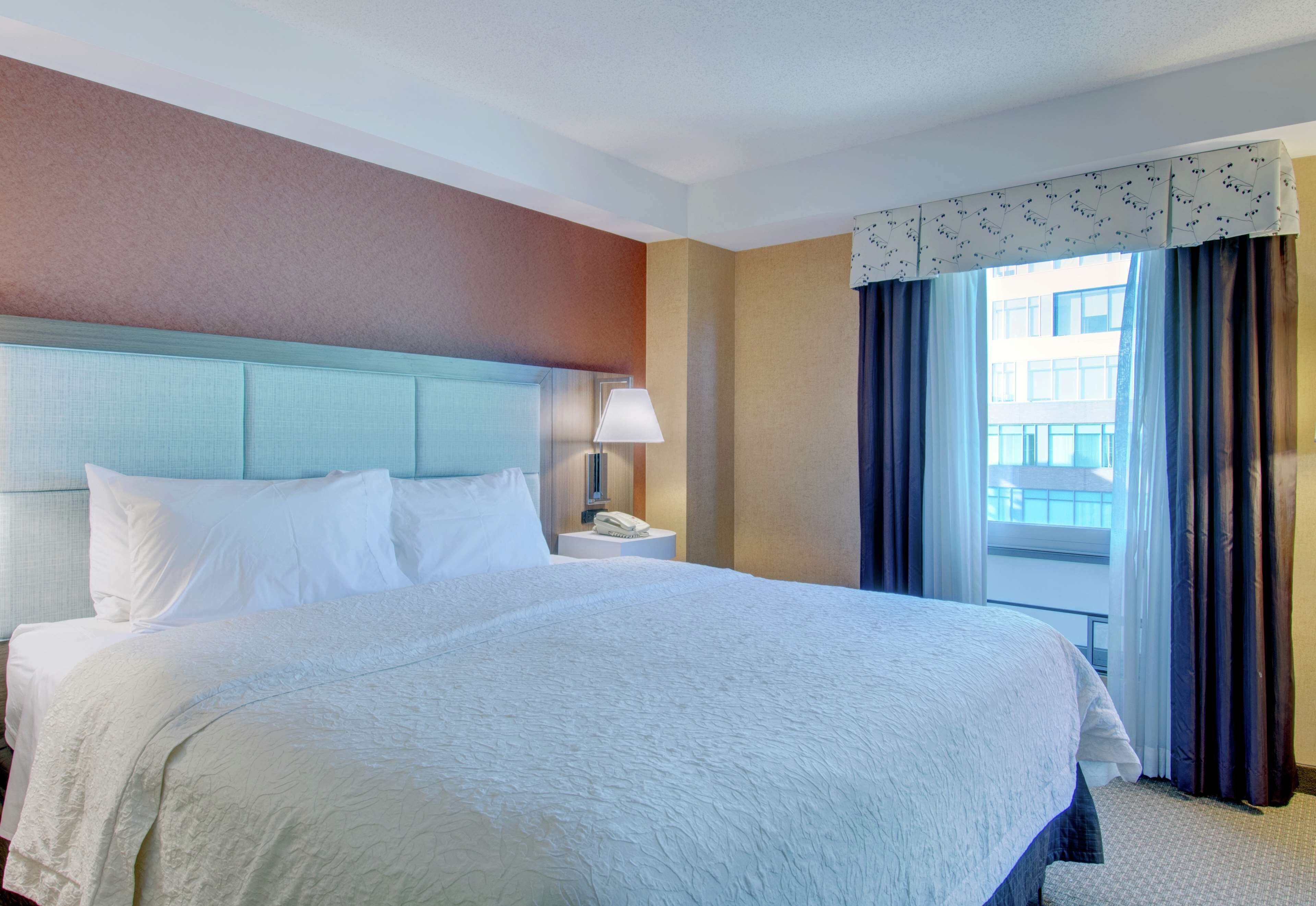 A hotel room with a large bed, a nightstand, a lamp, and a window with curtains.