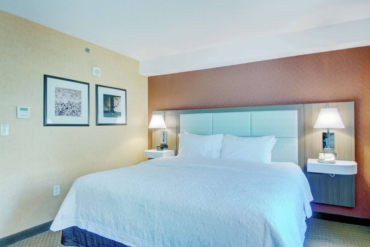 Una camera d'albergo con un letto grande, due comodini con lampade e due quadri appesi al muro.