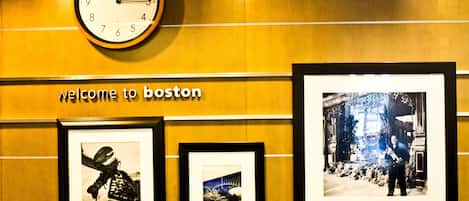 A wall with a clock, a 'Welcome to Boston' sign, and three framed photographs.