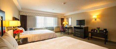 A hotel room with two beds, a desk, a chair, a television, and a lamp.