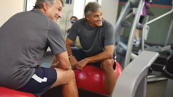 Twee mannen zitten op rode fitnessballen in een sportschool, met loopbanden op de achtergrond.