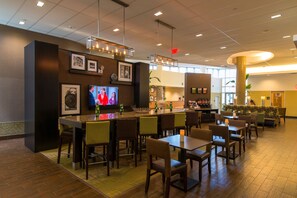 A modern bar area with a television, framed pictures, and a seating area with tables and chairs. - Hampton Inn & Suites Boston Crosstown Center (Boston)