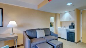 Habitació d'hotel senzilla amb un sofà, una taula petita amb una làmpada, i una cuineta equipada amb microones i nevera.