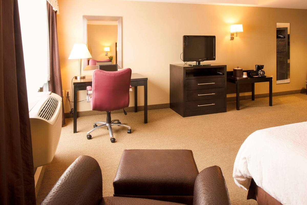 Una camera d'albergo con un letto, una scrivania con un computer, una sedia, una televisione, una macchina del caffè e una lampada.