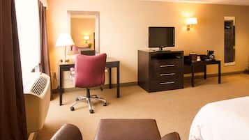 A hotel room with a bed, a desk with a computer, a chair, a television, a coffee maker, and a lamp.
