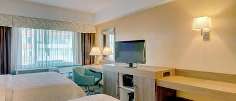 A hotel room with two beds, a desk with a television, a chair, and a lamp.
