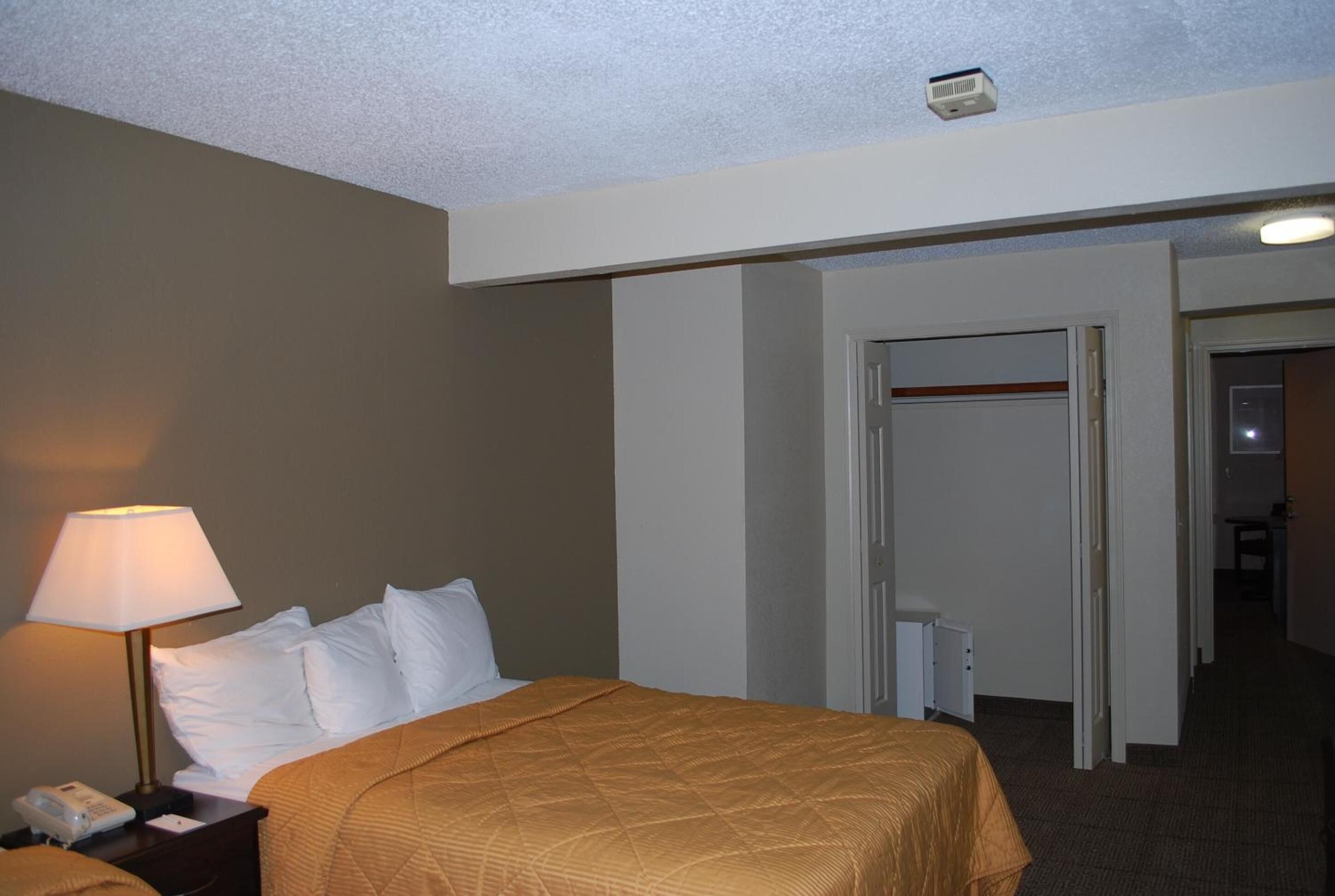 Une chambre d’hôtel avec un lit, une table de chevet avec une lampe, un téléphone et une porte donnant sur une autre pièce.