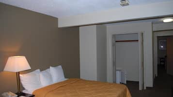 Une chambre d’hôtel avec un lit, une table de chevet avec une lampe, un téléphone et une porte donnant sur une autre pièce.