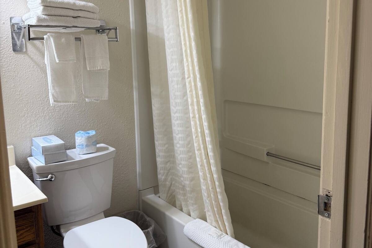 A bathroom with a toilet, a shower with a curtain, and a towel rack with towels.