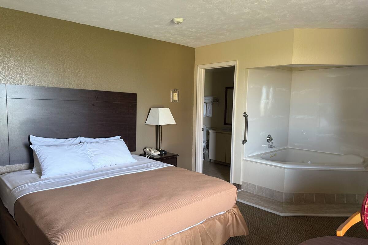 A hotel room with a large bed, a bedside lamp, a phone, a bathroom with a bathtub, and a shower.