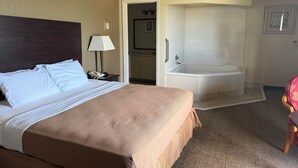 A hotel room with a large bed, a separate bathroom with a bathtub, a desk with a lamp, and a chair. - Clinton Inn And Suites (Port Clinton)
