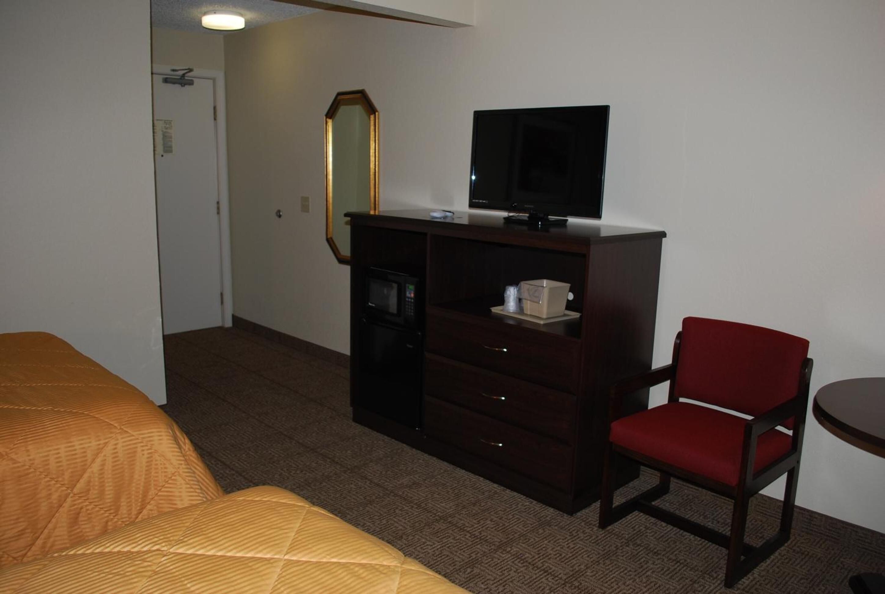 Quarto de hotel com cama, escrivaninha com televisão, cadeira e micro-ondas.