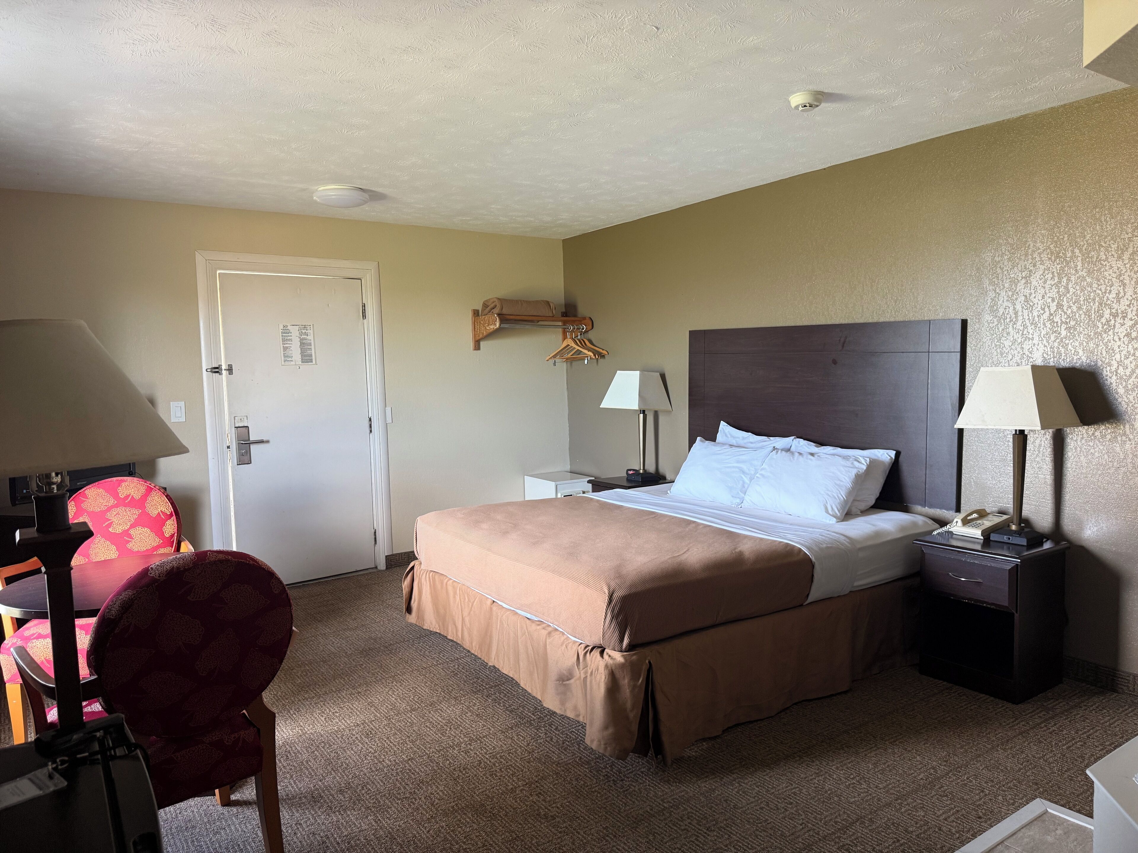 A hotel room with a bed, two bedside tables, a chair, a desk, and a door.