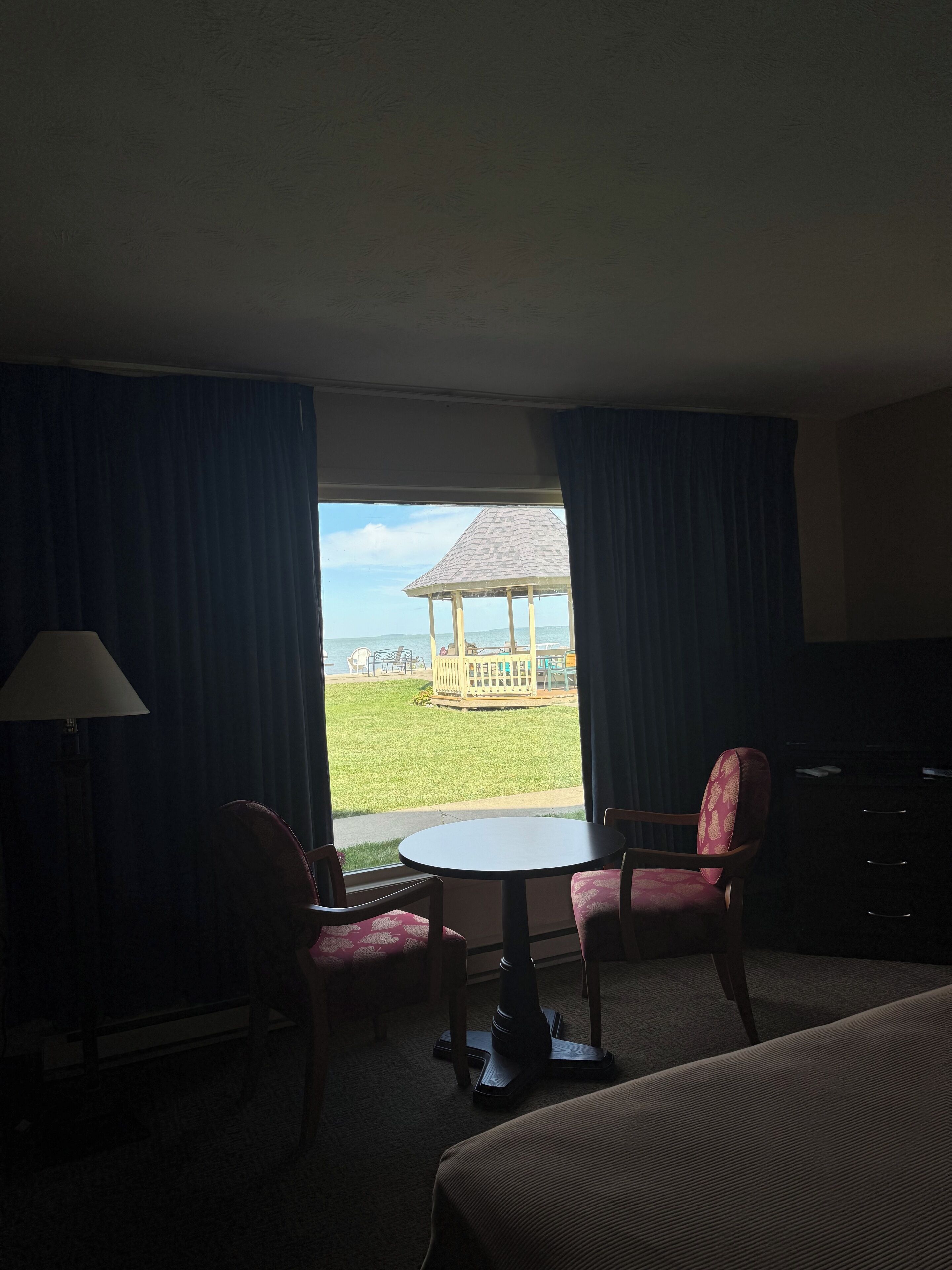 Habitación de hotel con cama, una mesa, dos sillas, una lámpara y vistas a un espacio exterior con un pabellón.