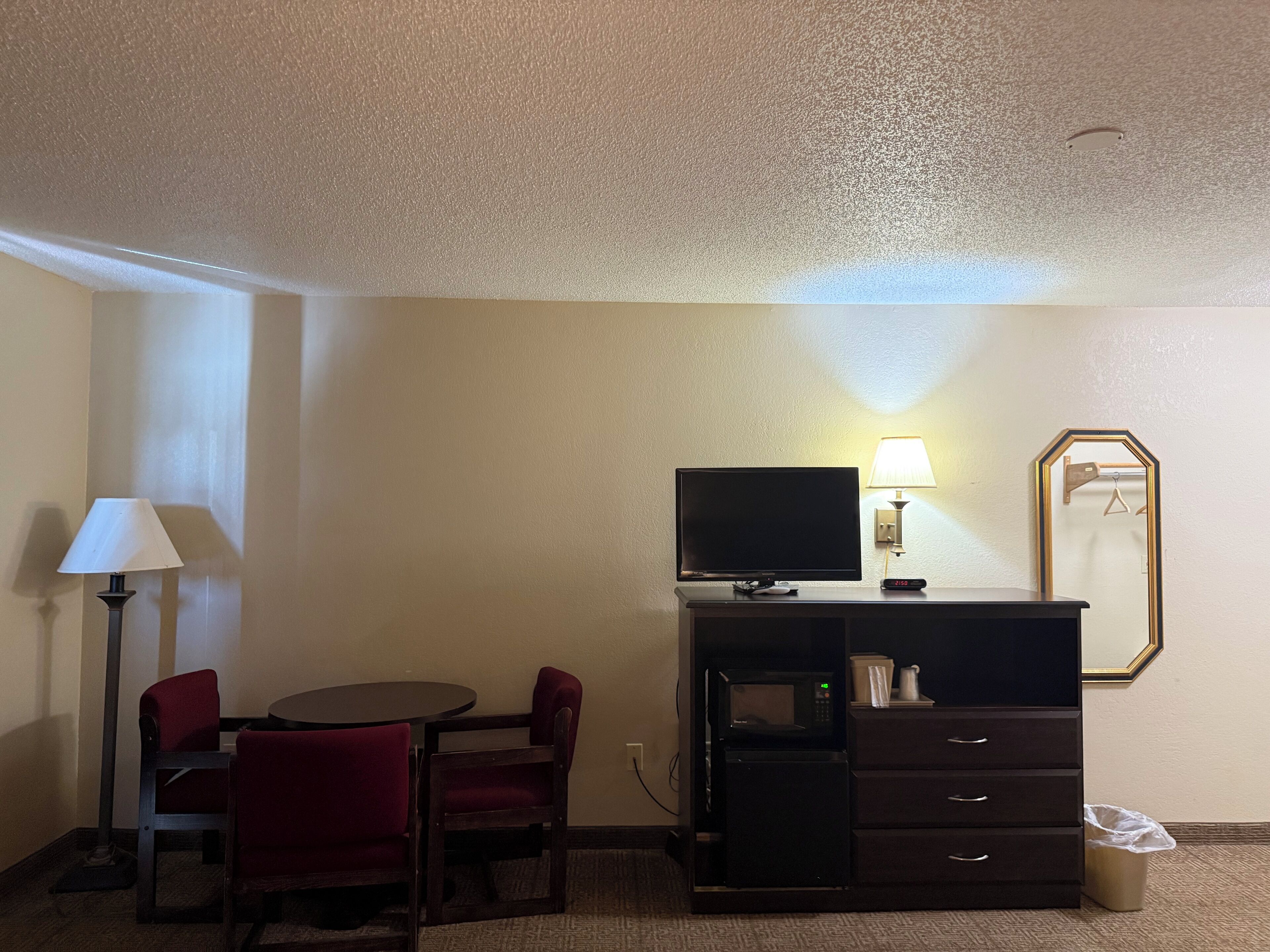 Habitación de hotel con televisor, lámpara y una pequeña mesa con sillas.