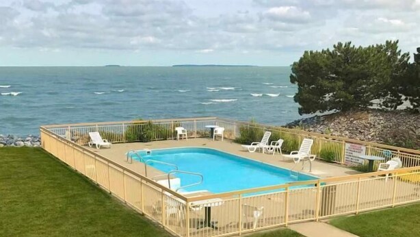 A rectangular swimming pool with a wooden deck, surrounded by white lounge chairs and a safety fence. - Clinton Inn And Suites (Port Clinton)