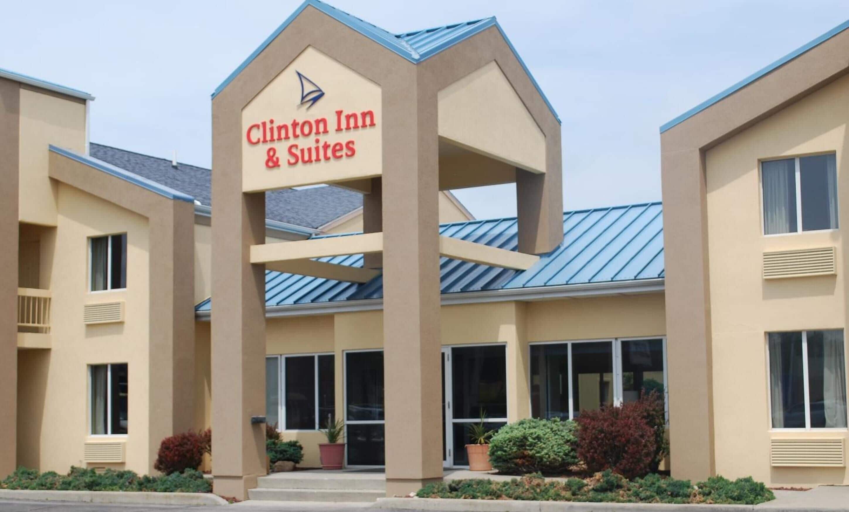 Un hôtel appelé Clinton Inn & Suites, doté d’une architecture moderne, se distingue par son entrée imposante et offre une vue dégagée sur la façade du bâtiment.