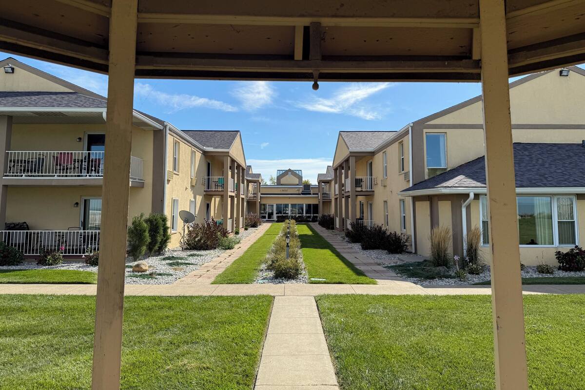 A covered walkway leading to a row of townhouses with balconies and a central lawn area.
