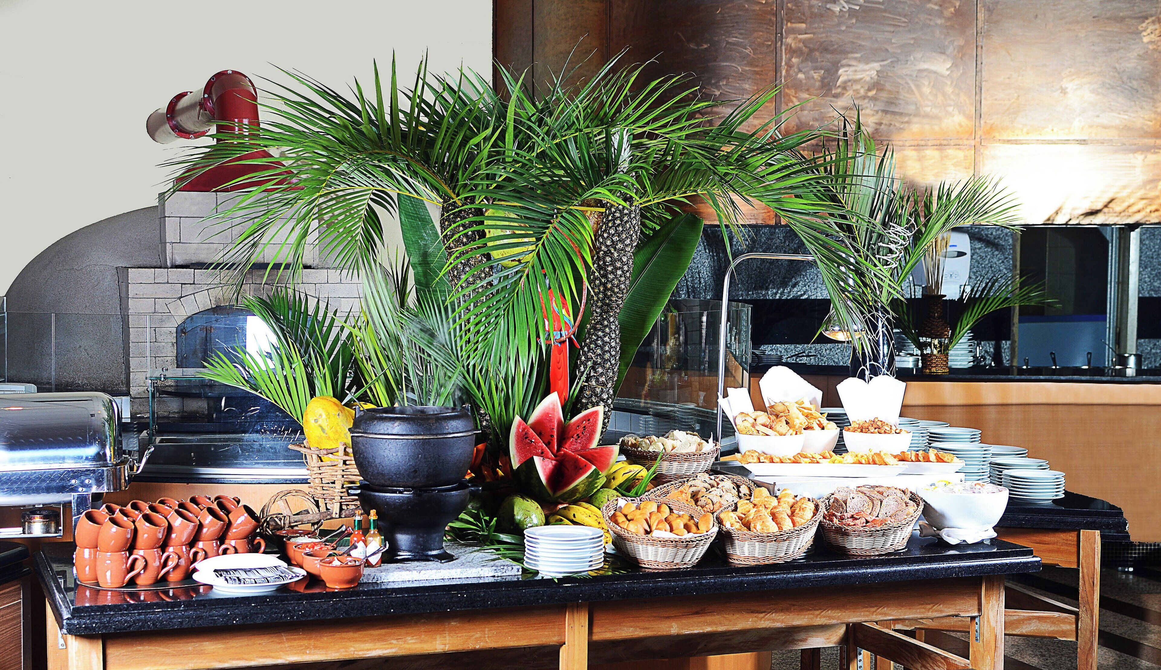 Una mesa de buffet con diversos alimentos, como frutas, pan y pastelería, y una máquina de café al fondo.