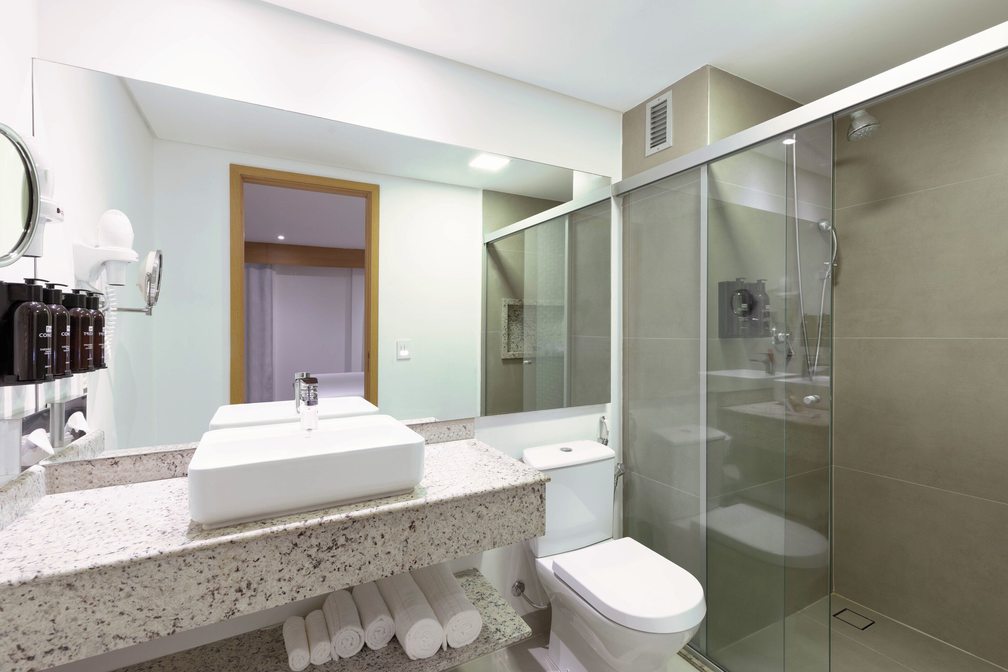 Een moderne badkamer met een wastafel met een granieten blad, een glazen douchecabine en een toilet.