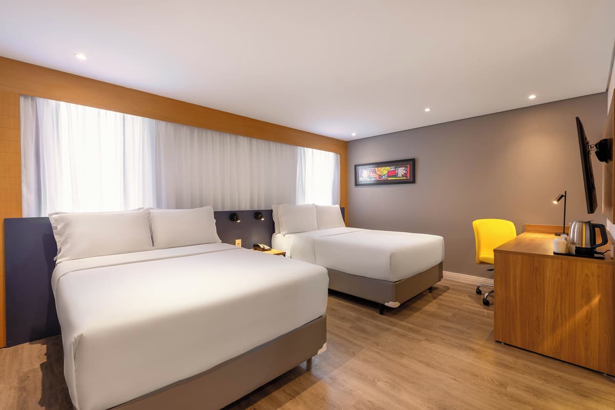 Una habitación de hotel con dos camas, un escritorio con tetera y una silla amarilla.