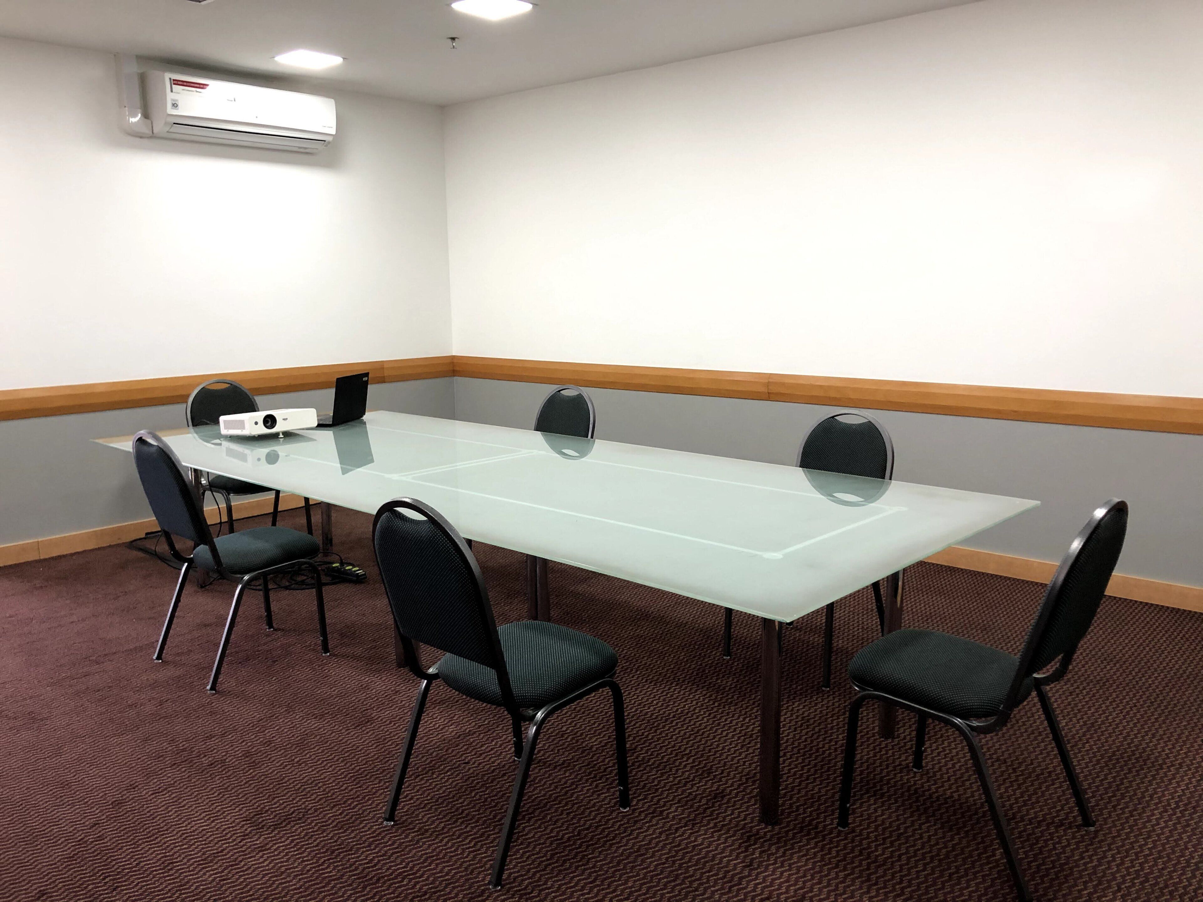 A conference room with a glass table, black chairs, a projector, and an air conditioning unit.