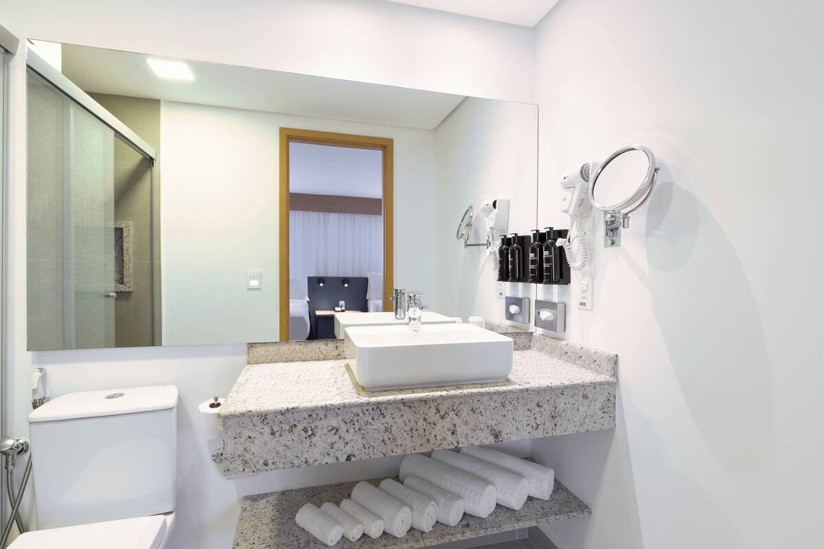 Un baño moderno con un espejo grande, un lavamanos blanco y un perchero para toallas.
