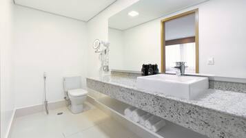A modern bathroom with a white toilet, a sink with a large mirror above it, and a shower area.